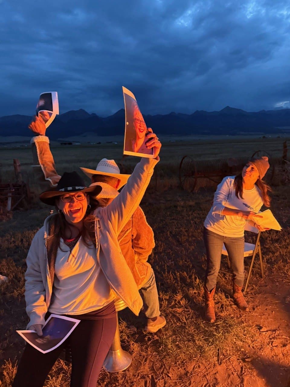 Women's group activity at dusk at Turkey Toe — holding up photos lit by warm fire glow with the Sangre de Cristo mountains behind them