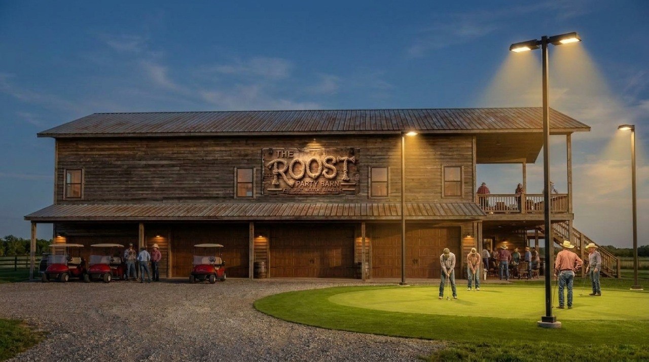 The Roost Party Barn at dusk with golfers putting outside β golf carts lined up, guests on the upper deck, party barn sign lit up